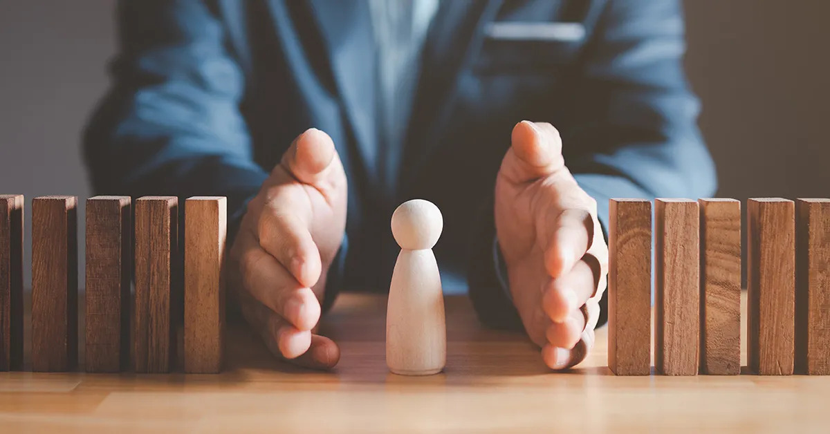A man holding both hands vertically with a human figurine in between and domino blocks on both sides