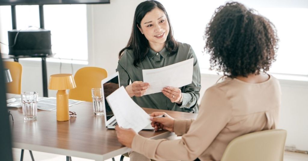 Woman with a paper in her hands while looking at another woman across the table