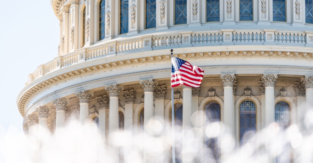 U.S. Congress dome closeup with background of water fountain splashing and American flag waving