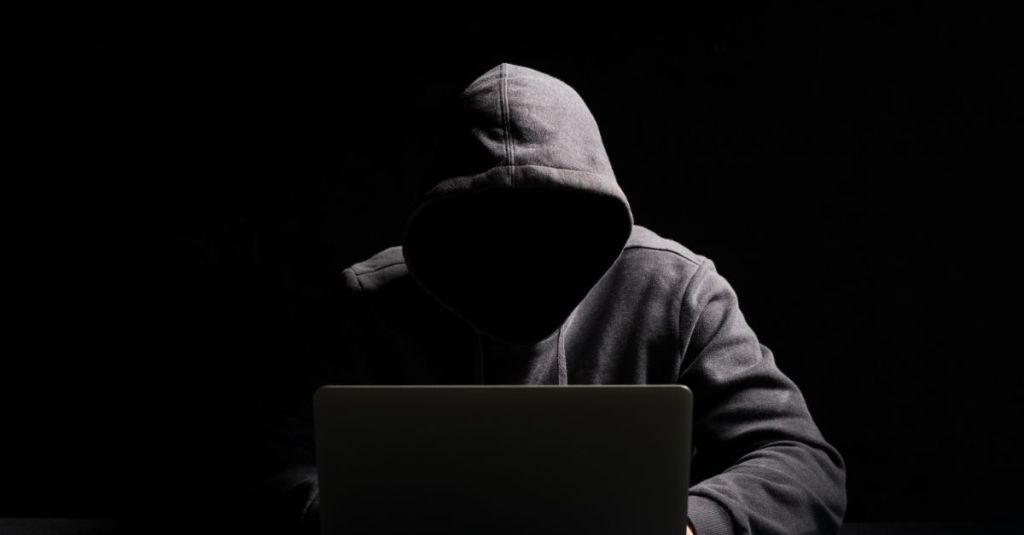 Person with a hoodie on a laptop in a dark room