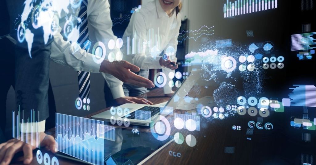 People talking at a desk with laptops and digital icons across the image