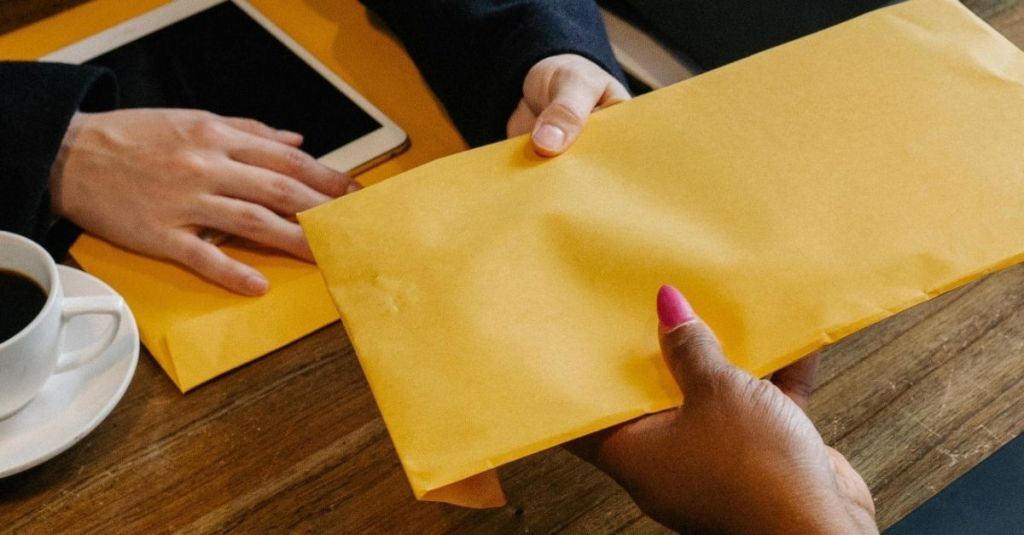 Man handing off a yellow envelope of papers to a woman