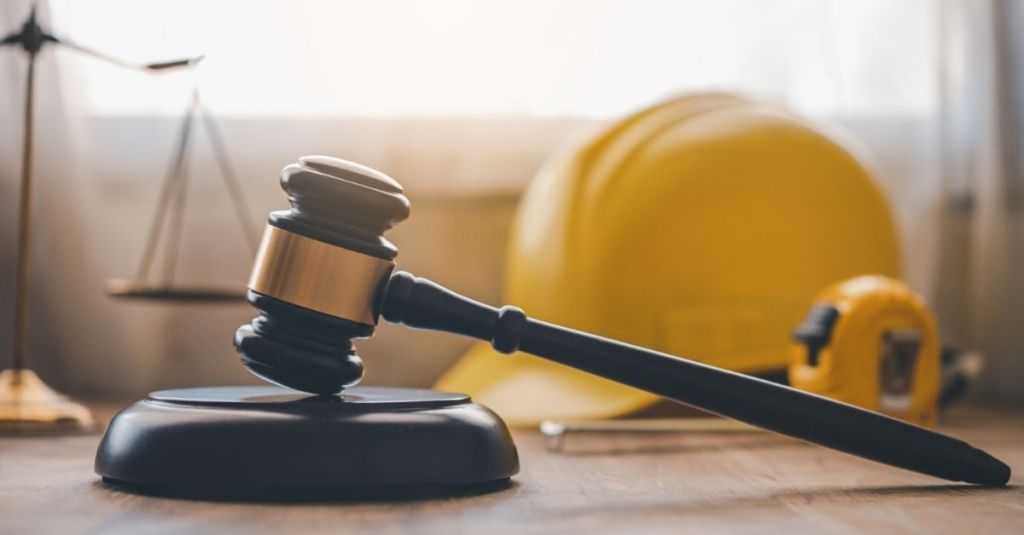 A gavel sitting in front of a yellow hard hat and tape measure