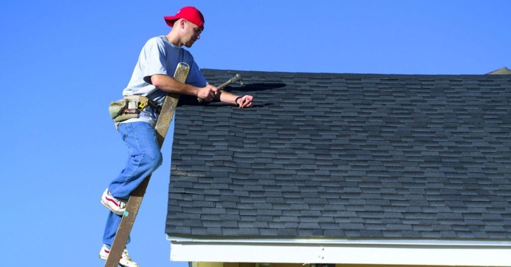 Man at the top of a ladder that's leaning against the roof of a house