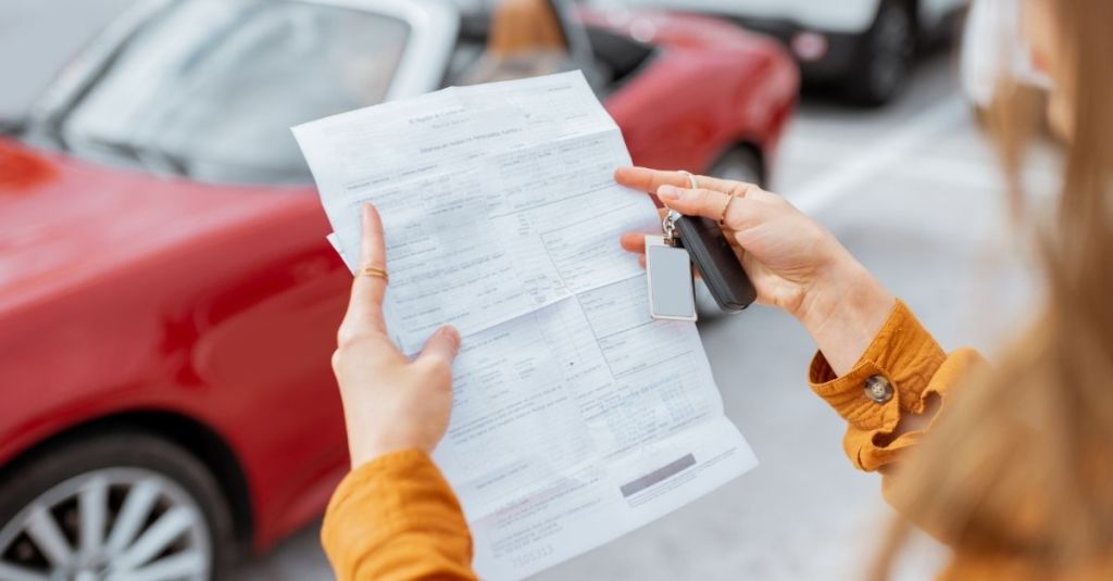 Lady looking at document in front of a red car