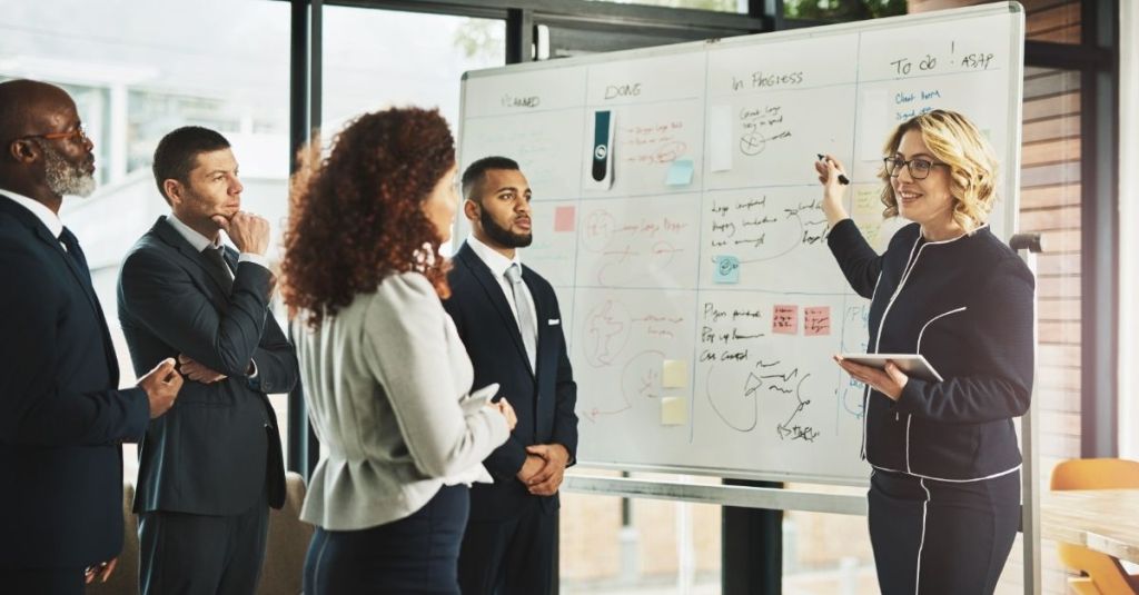 Team leader pointing at a white board in front of four team members