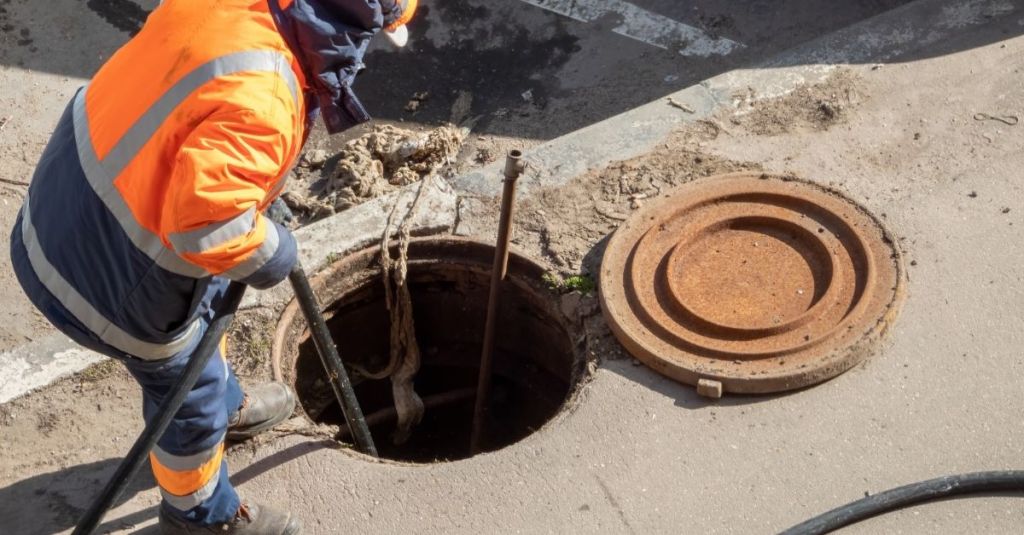 Construction worker holding a tube that's going down a manhole
