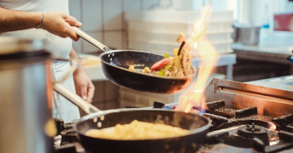 Cook tossing food in a pan in a commercial kitchen