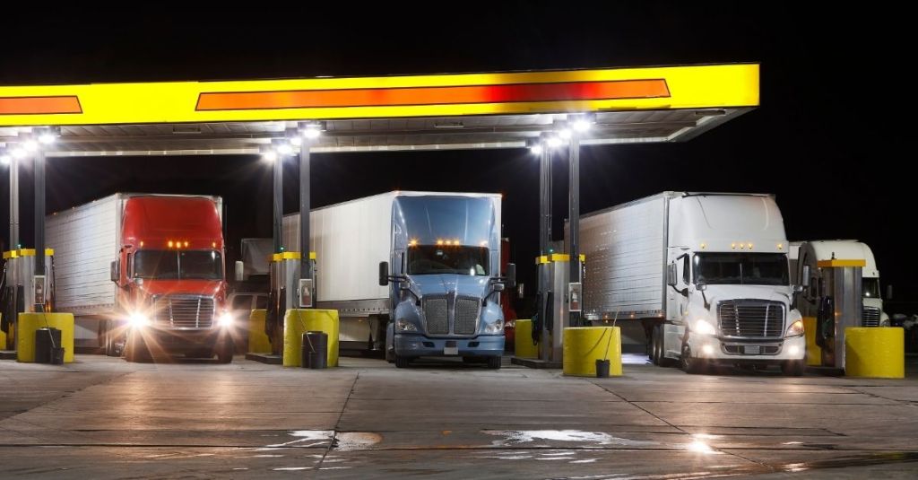 Three semi-trailer trucks lined up at gas pumps at a truck stop