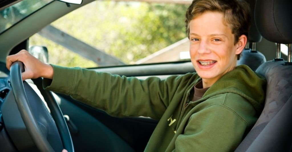 Young boy smiling at the camera while the steering wheel in a car