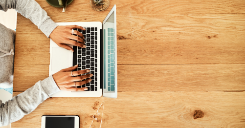 Hands typing on a laptop with coffee and phone