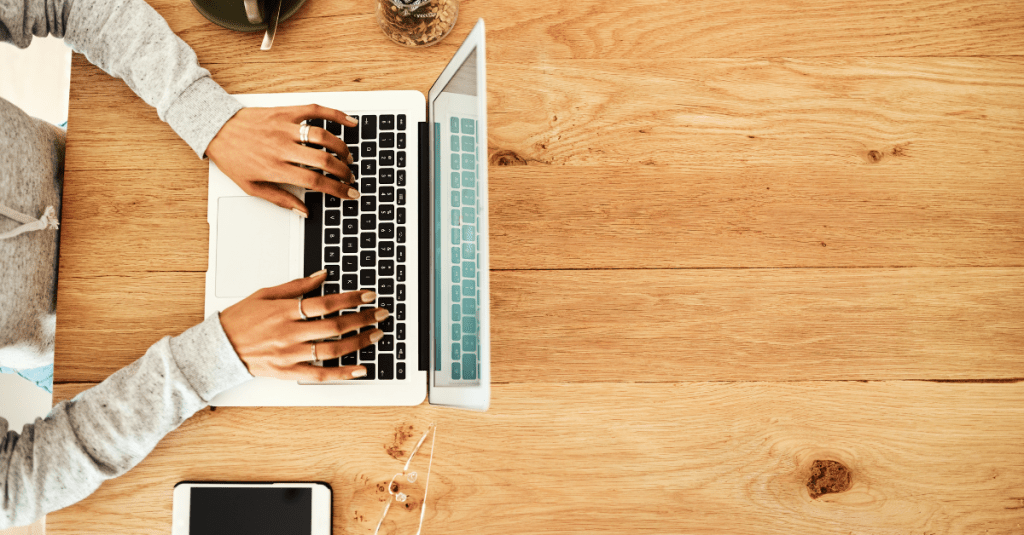 Hands typing on a laptop with coffee and phone