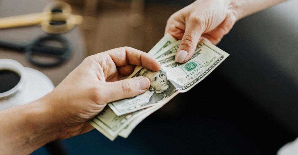 A person handing off twenty-dollar bills to another person.