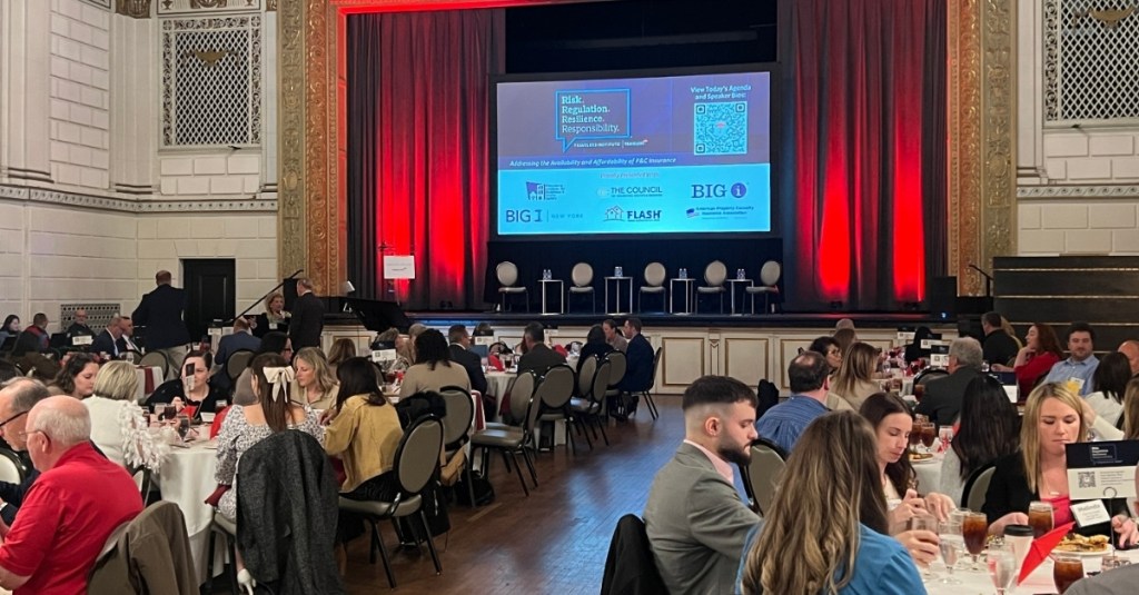 Stage and crowd view of the 2026 Travelers Institute Symposium.